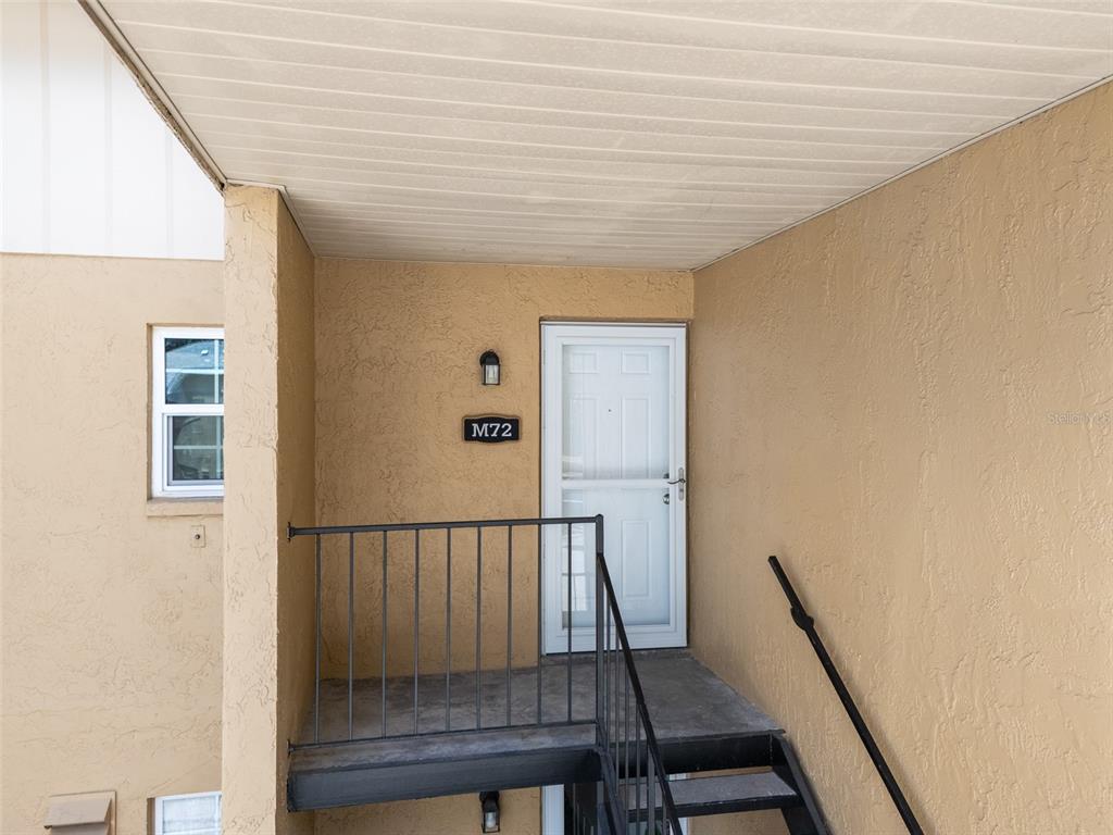A tan stucco building exterior features a white front door labeled M72 and metal stairs — 3812 N OAK DRIVE UNIT M72, TAMPA, FL