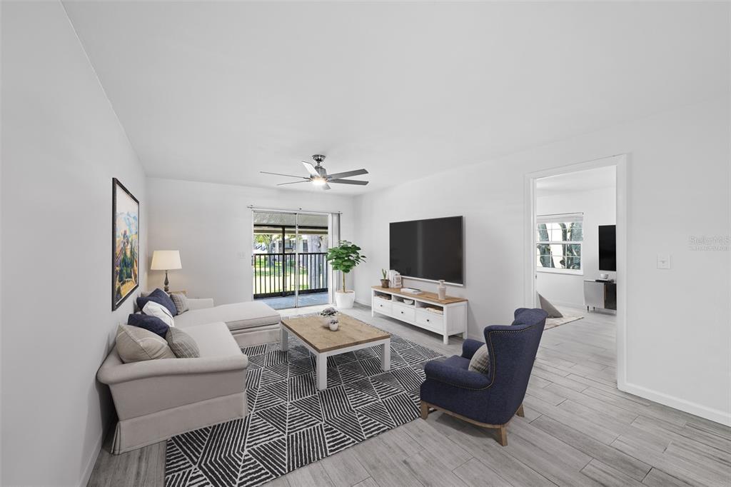 A living room features a sectional sofa, blue armchair, television, and sliding glass patio doors — 3812 N OAK DRIVE UNIT M72, TAMPA, FL