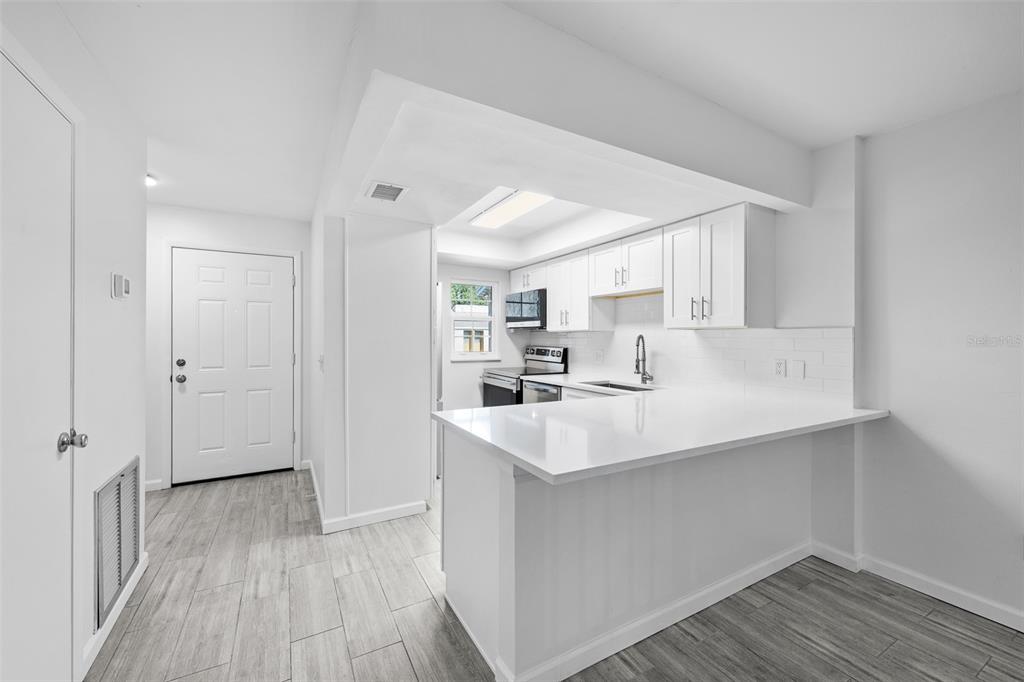 A modern kitchen features white cabinets, a breakfast bar, and light gray wood-look flooring — 3812 N OAK DRIVE UNIT M72, TAMPA, FL