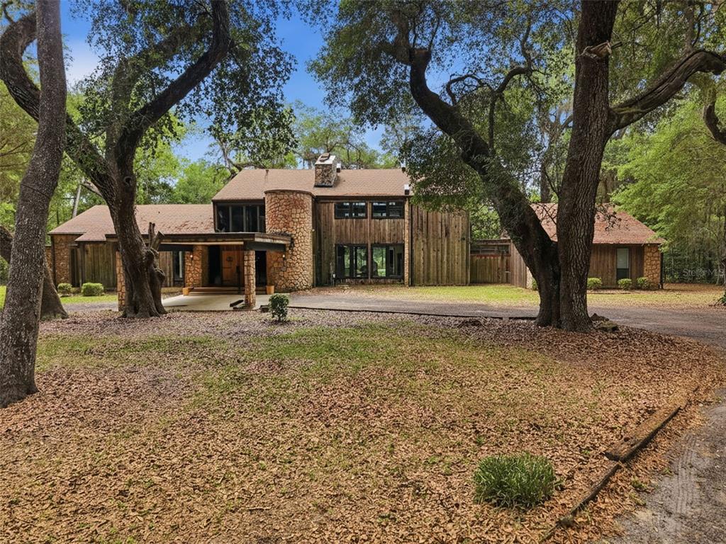 A two-story wood-sided house with a stone chimney and circular tower sits among large trees — 16650 NE 53RD LANE, WILLISTON, FL