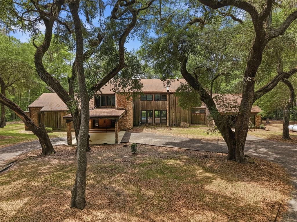 A two-story house with wood siding and stone accents sits among large oak trees — 16650 NE 53RD LANE, WILLISTON, FL