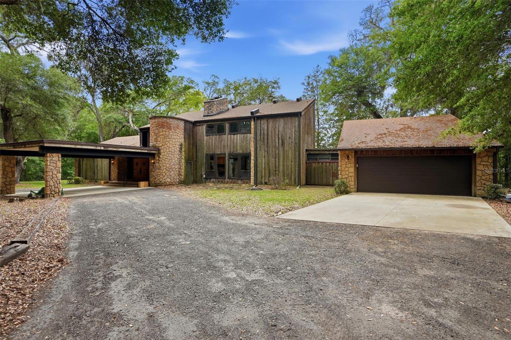 A two-story house with vertical wood siding, stone accents, a carport, and a detached garage — 16650 NE 53RD LANE, WILLISTON, FL