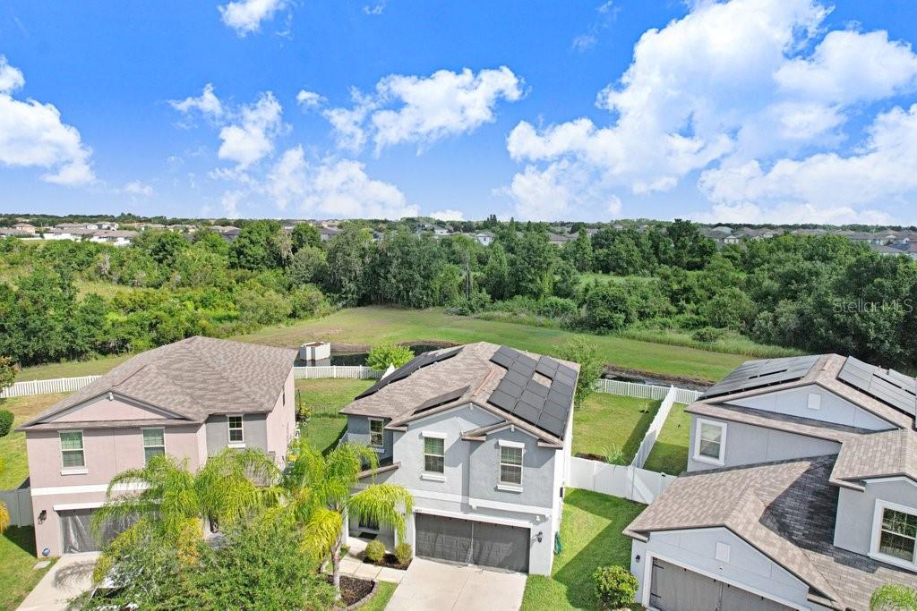 An aerial view shows three suburban houses with solar panels and a backyard pond area — 14855 CRESCENT ROCK DRIVE, WIMAUMA, FL
