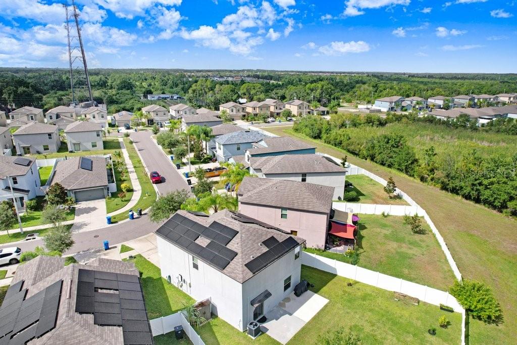 An aerial view shows several suburban houses with solar panels and fenced backyards — 14855 CRESCENT ROCK DRIVE, WIMAUMA, FL