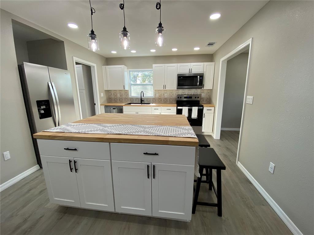 A kitchen features white cabinets, a wood-topped island, stainless steel appliances, and gray flooring — 12704 LACEY DRIVE, NEW PORT RICHEY, FL