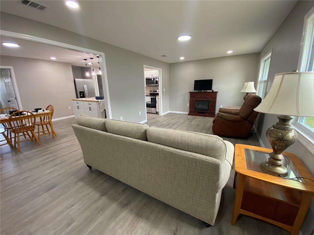 A living room with light wood-look flooring, a beige sofa, and a fireplace with television — 12704 LACEY DRIVE, NEW PORT RICHEY, FL