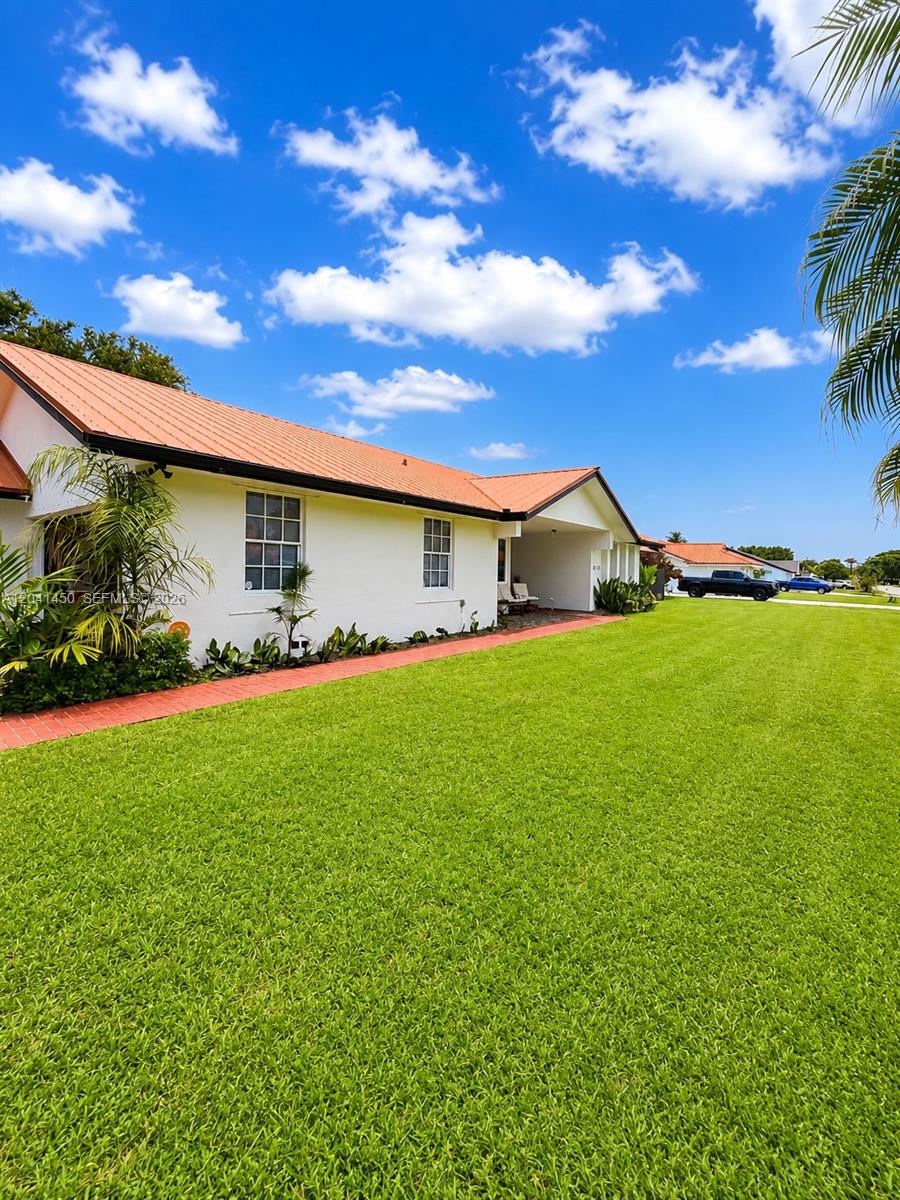 A white house with a terracotta-colored roof sits beside a large, manicured green lawn — 18740 SW 294th Ter, Homestead FL 33030, HOMESTEAD, FL