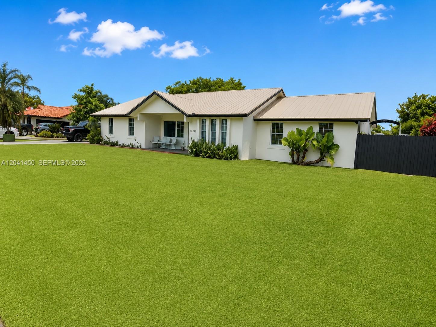 A single-story house with a light-colored exterior and a metal roof sits on a lawn — 18740 SW 294th Ter, Homestead FL 33030, HOMESTEAD, FL