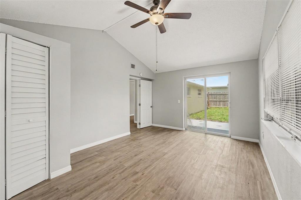 An empty room with light wood-look flooring, a vaulted ceiling, and sliding glass patio doors — 5102 SCHOOL ROAD, NEW PORT RICHEY, FL