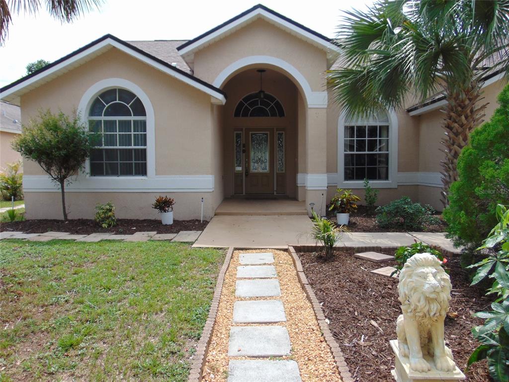 A beige single-story house features an arched entryway, a stone walkway, and a lion statue — 3126 SAMOSA HILL CIRCLE, CLERMONT, FL