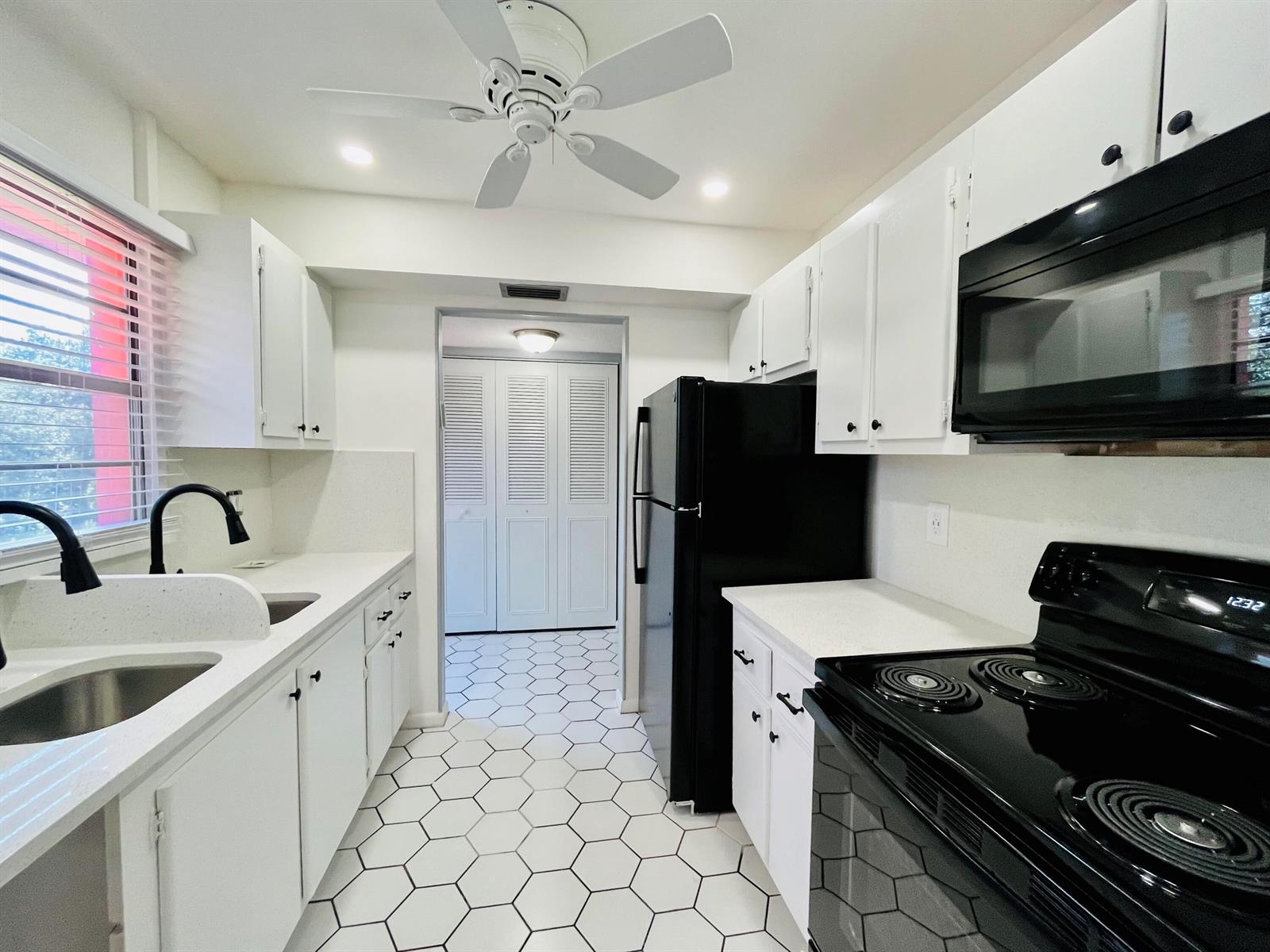 A galley kitchen features white cabinets, black appliances, quartz countertops, and white hexagonal floor tiles — 11 Golfs Edge E, West Palm Beach FL 33417, WEST PALM BEACH, FL