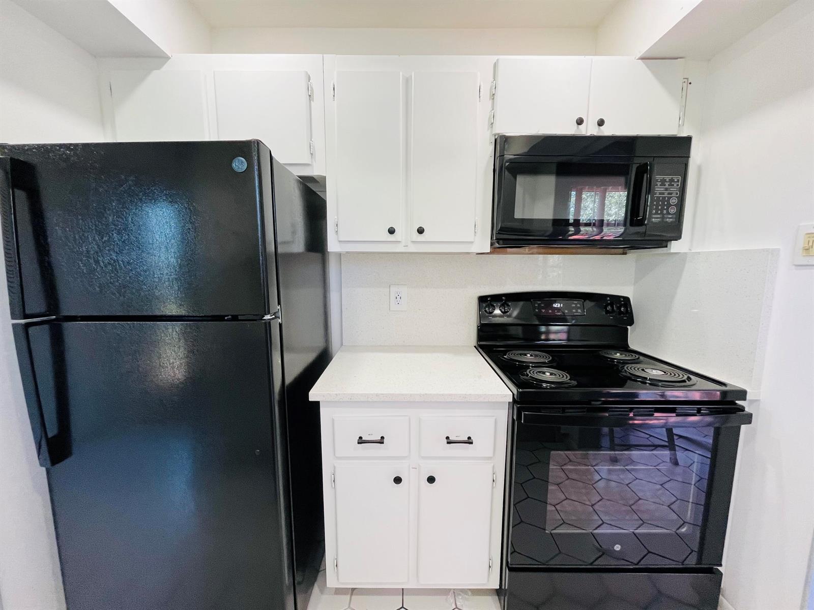 A kitchen features white cabinets, a black refrigerator, a black stove, and a black microwave — 11 Golfs Edge E, West Palm Beach FL 33417, WEST PALM BEACH, FL