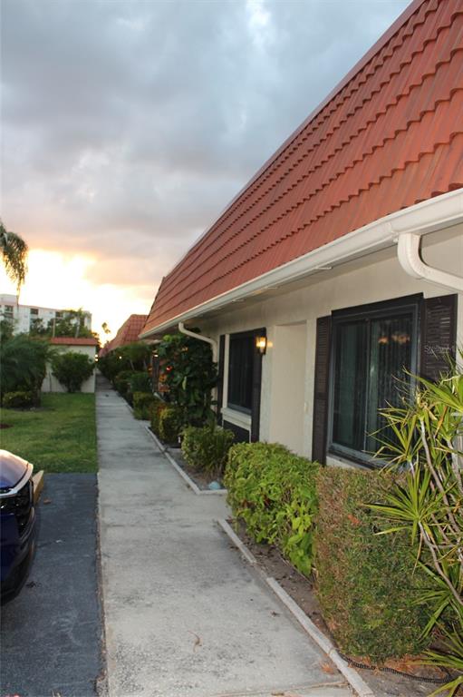 A sidewalk runs alongside a single-story building with a red tiled roof and landscaping — 19029 US HIGHWAY 19 N UNIT 16C, CLEARWATER, FL