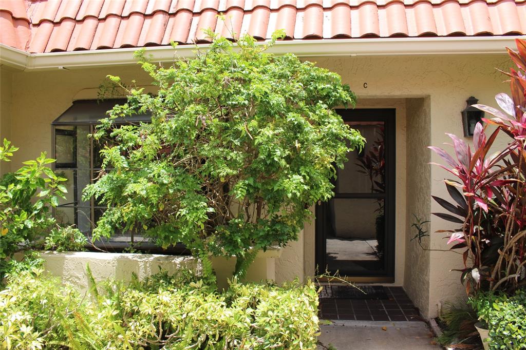 The exterior of a residential unit features a tiled roof, a front door, and landscaping — 19029 US HIGHWAY 19 N UNIT 16C, CLEARWATER, FL