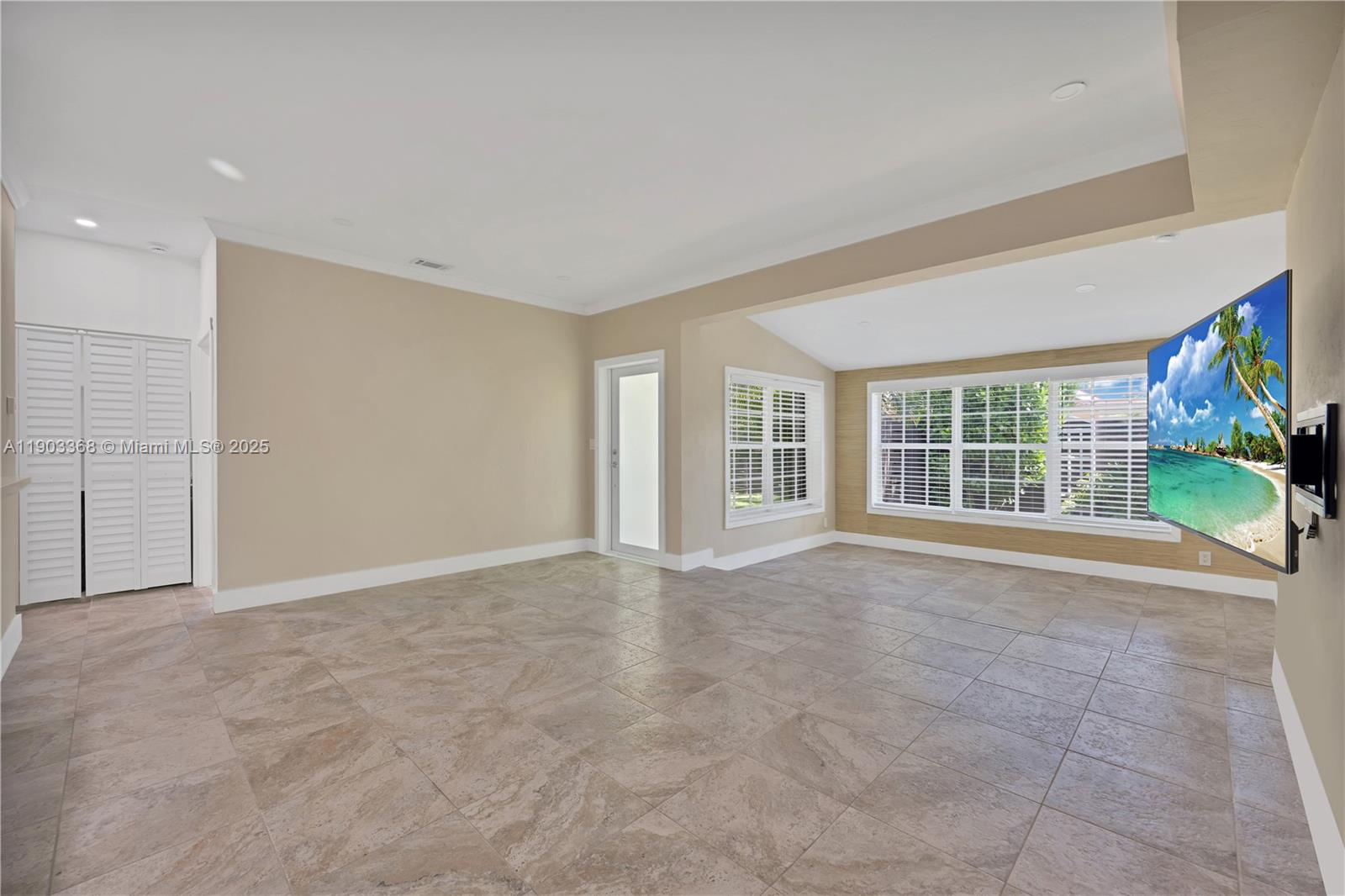 A spacious living room features beige walls, large tile flooring, and a wall-mounted television — 818 NE 3rd St, Hallandale Beach FL 33009, HALLANDALE BEACH, FL