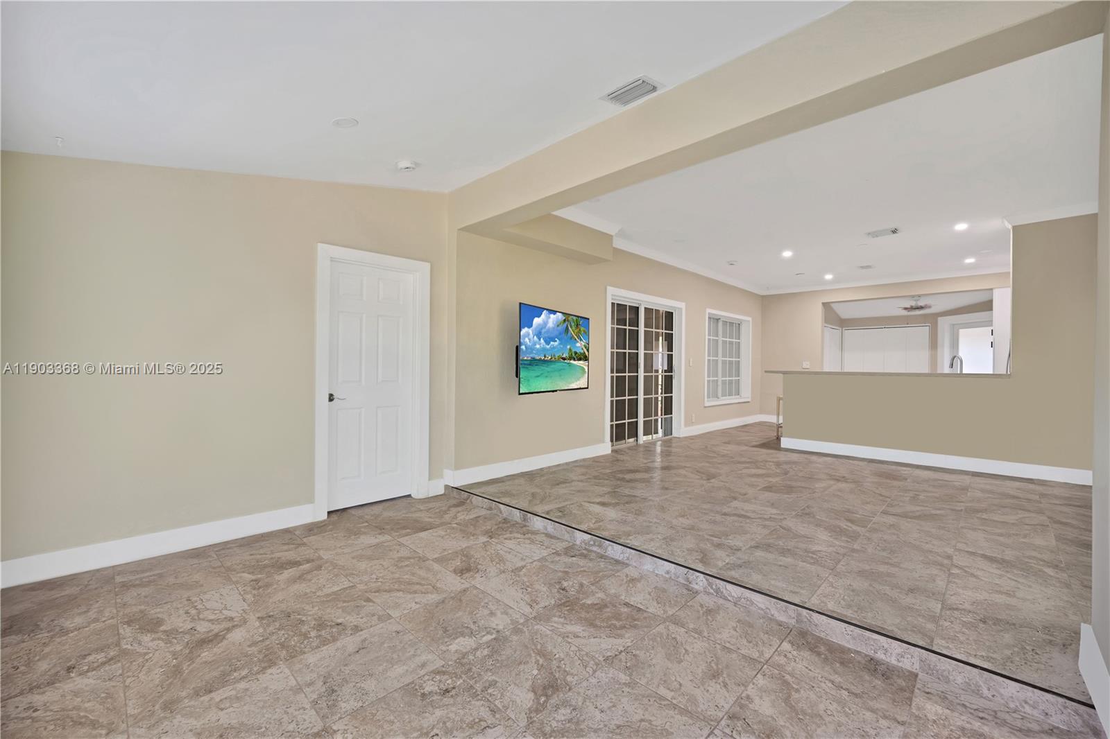 A living area with tile flooring, a wall-mounted television, and an adjacent kitchen counter — 818 NE 3rd St, Hallandale Beach FL 33009, HALLANDALE BEACH, FL