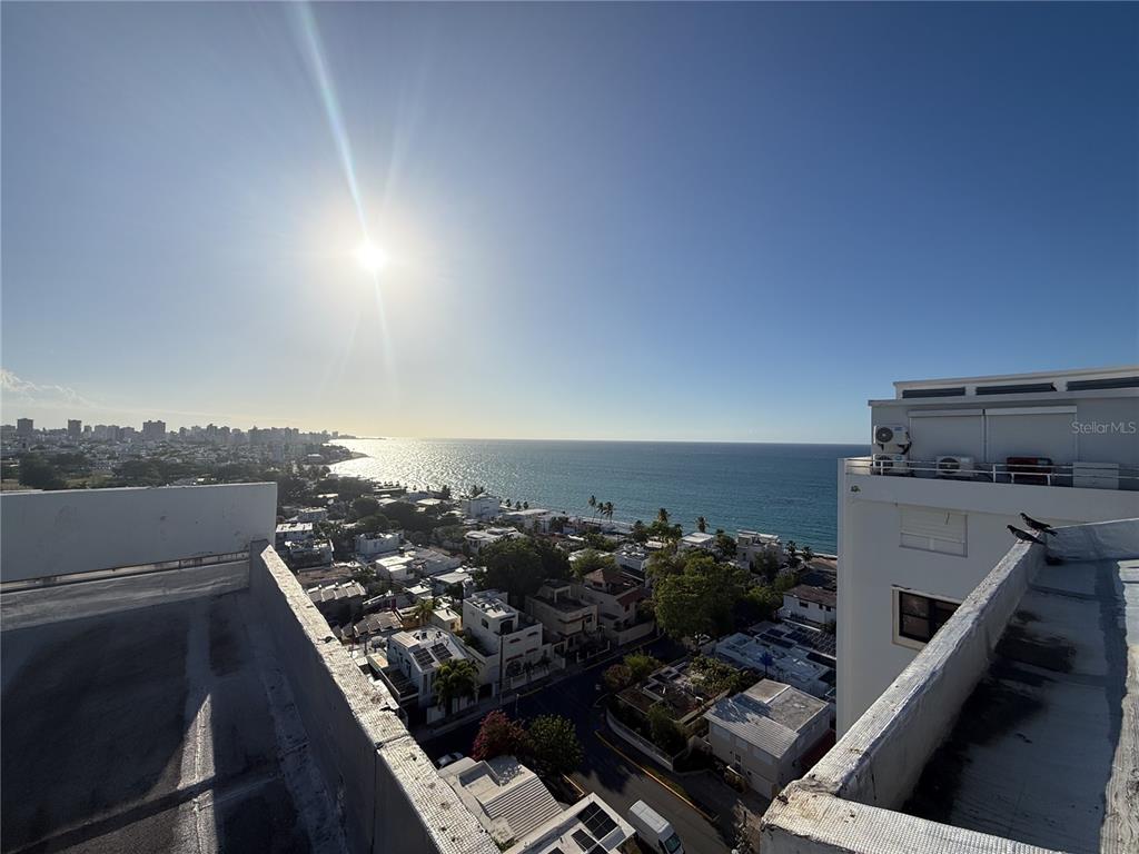 An elevated view of a coastal city with buildings, trees, and the ocean under sunlight — . LAUREL UNIT 2306, SAN JUAN, PR