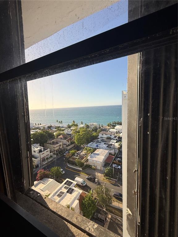 A high-angle view through a window shows a coastal neighborhood and the ocean beyond — . LAUREL UNIT 2306, SAN JUAN, PR