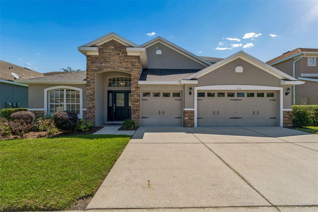 A single-story suburban house with a stone-accented entryway, two garage doors, and a concrete driveway — 2336 NESSLEWOOD DRIVE, WESLEY CHAPEL, FL