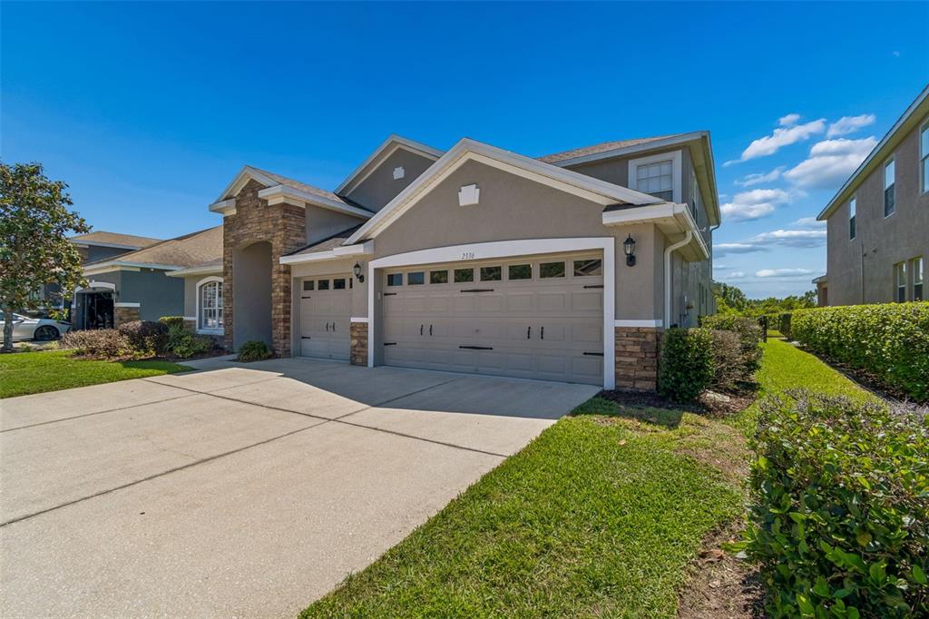 A two-story suburban house features a stone-accented facade, a three-car garage, and a concrete driveway — 2336 NESSLEWOOD DRIVE, WESLEY CHAPEL, FL