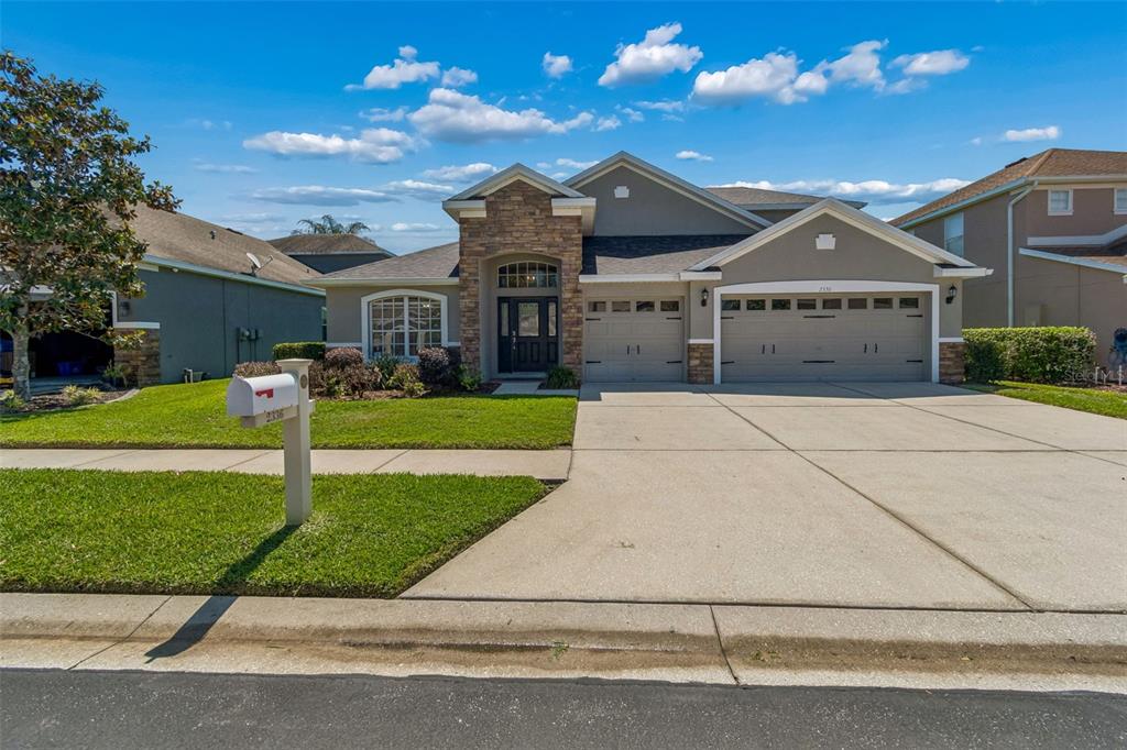 A single-story suburban house with a stone facade, a three-car garage, and a manicured lawn — 2336 NESSLEWOOD DRIVE, WESLEY CHAPEL, FL