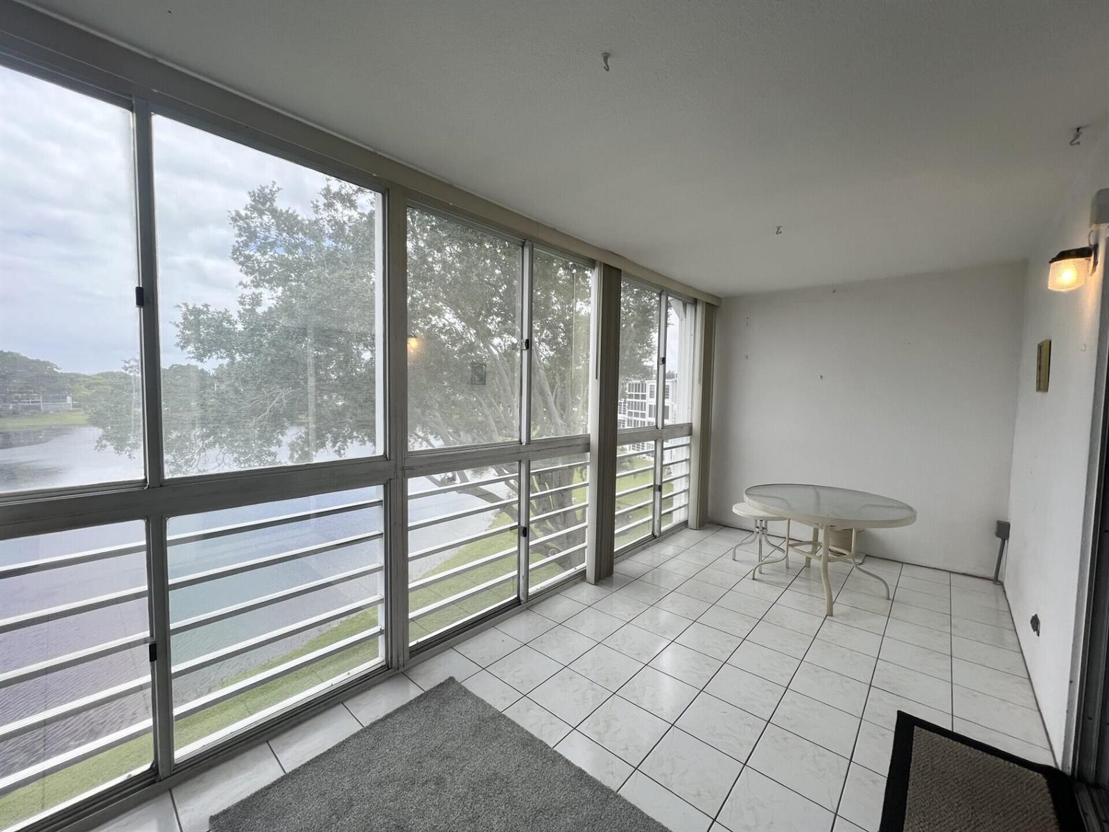 A sunroom with white tile flooring, large windows overlooking a lake, and a small table — 4116 Cambridge E, Deerfield Beach FL 33442, DEERFIELD BEACH, FL