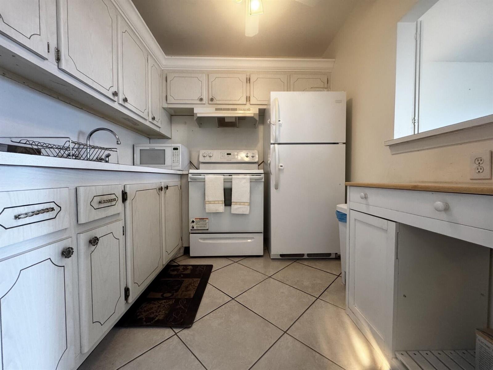 A small kitchen features white cabinets, white appliances, and light-colored tile flooring — 4116 Cambridge E, Deerfield Beach FL 33442, DEERFIELD BEACH, FL