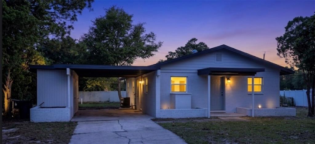 A single-story house with a carport, white brick exterior, and a small front porch at dusk — 1011 MONTCLAIR ROAD, COCOA, FL