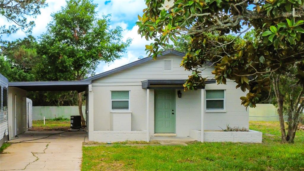 A single-story house with a light-colored exterior, a green front door, and an attached carport — 1011 MONTCLAIR ROAD, COCOA, FL
