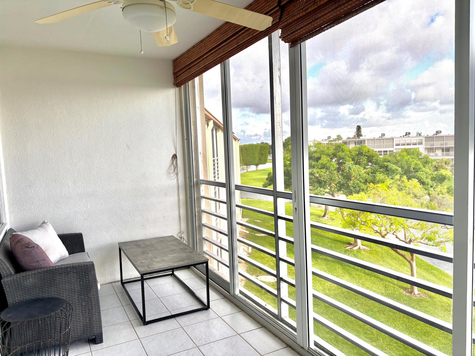 A screened-in balcony with tile flooring, a ceiling fan, wicker furniture, and a golf course view — 4032 Newcastle B, Boca Raton FL 33434, BOCA RATON, FL