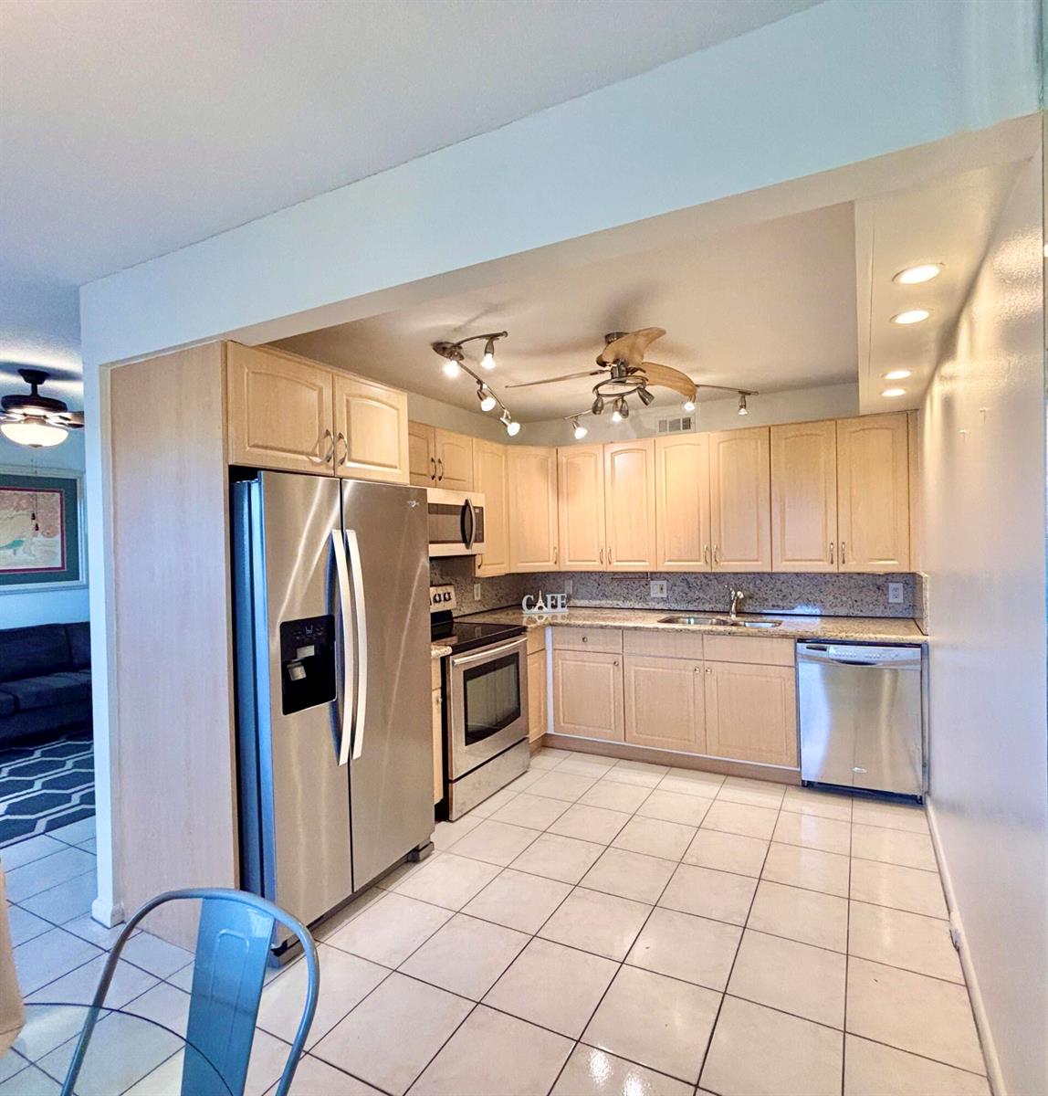 A kitchen features light wood cabinets, stainless steel appliances, granite countertops, and white tile flooring — 4032 Newcastle B, Boca Raton FL 33434, BOCA RATON, FL