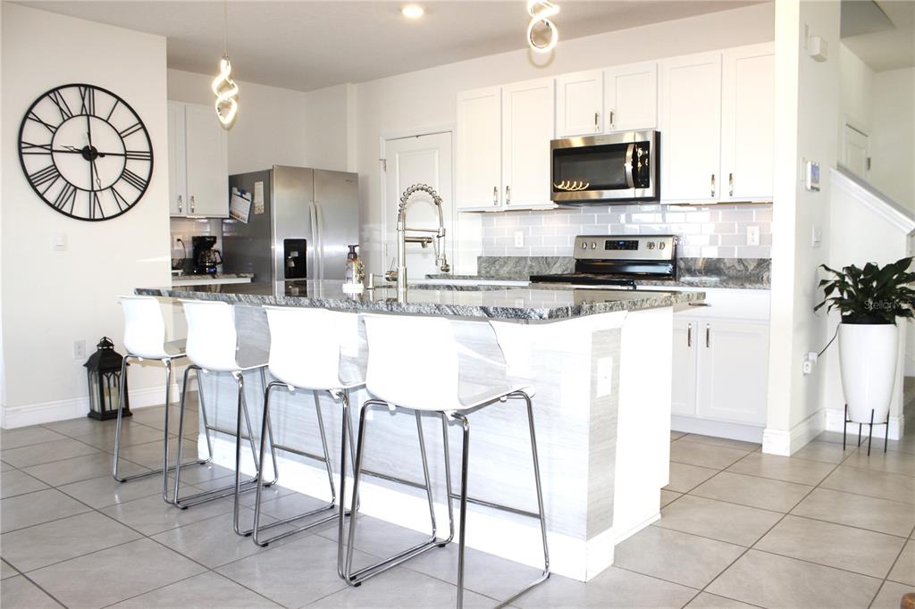 A modern kitchen features white cabinets, granite countertops, a central island, and four bar stools — 8406 HARDY BAY LOOP, WESLEY CHAPEL, FL