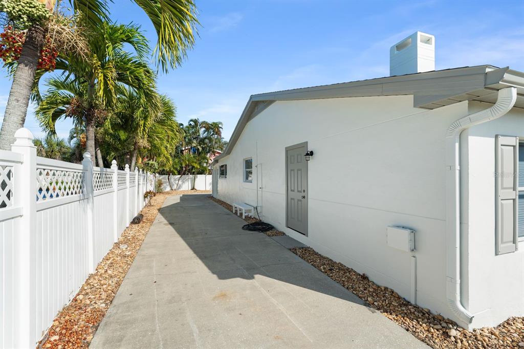 A concrete driveway runs alongside the white exterior wall of a house with a door — 107 4TH STREET, BELLEAIR BEACH, FL