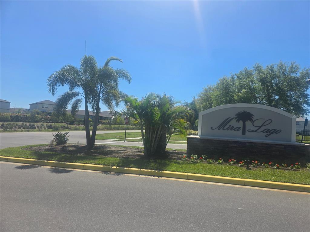 A stone monument sign for Mira Lago stands near palm trees and a paved road — 563 VISTA RIDGE DRIVE, RUSKIN, FL
