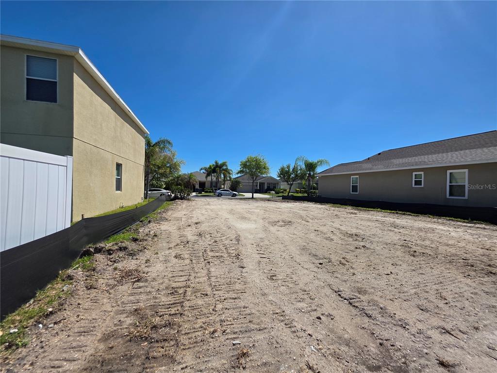 A vacant, cleared residential lot sits between two existing houses under a clear blue sky — 563 VISTA RIDGE DRIVE, RUSKIN, FL