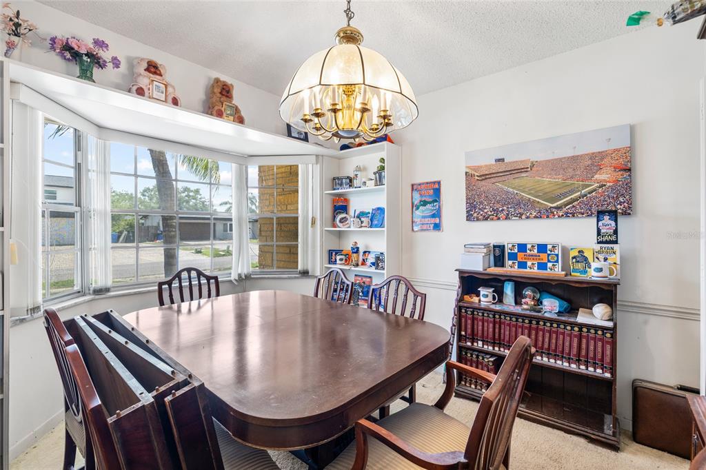 A dining room features a wooden table, chairs, a bookshelf, and a large bay window — 4709 TRAVERTINE DRIVE, TAMPA, FL