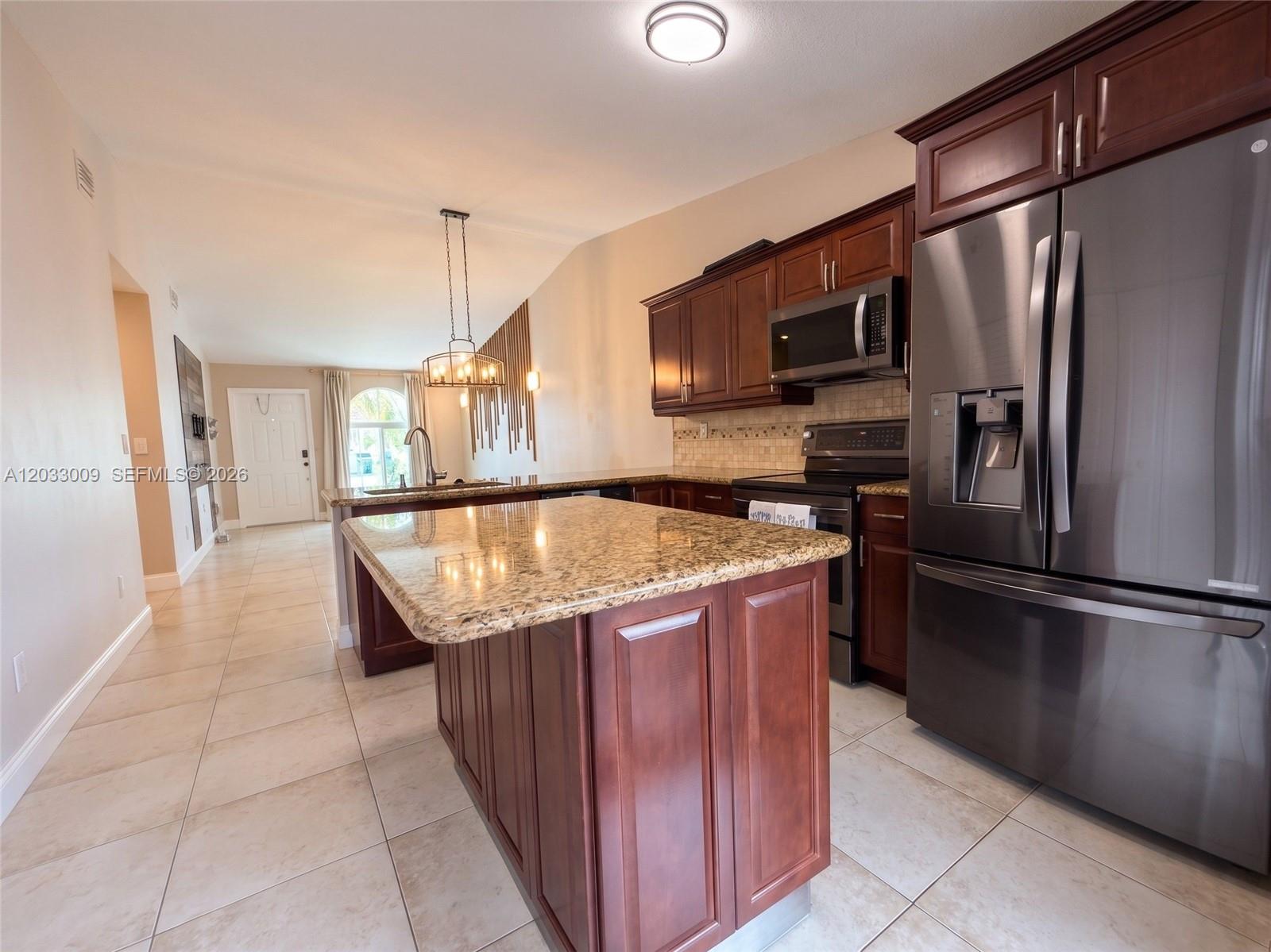 A kitchen features dark wood cabinets, granite countertops, a center island, and stainless steel appliances — 7675 NW 181st St # 7675, Hialeah FL 33015, HIALEAH, FL