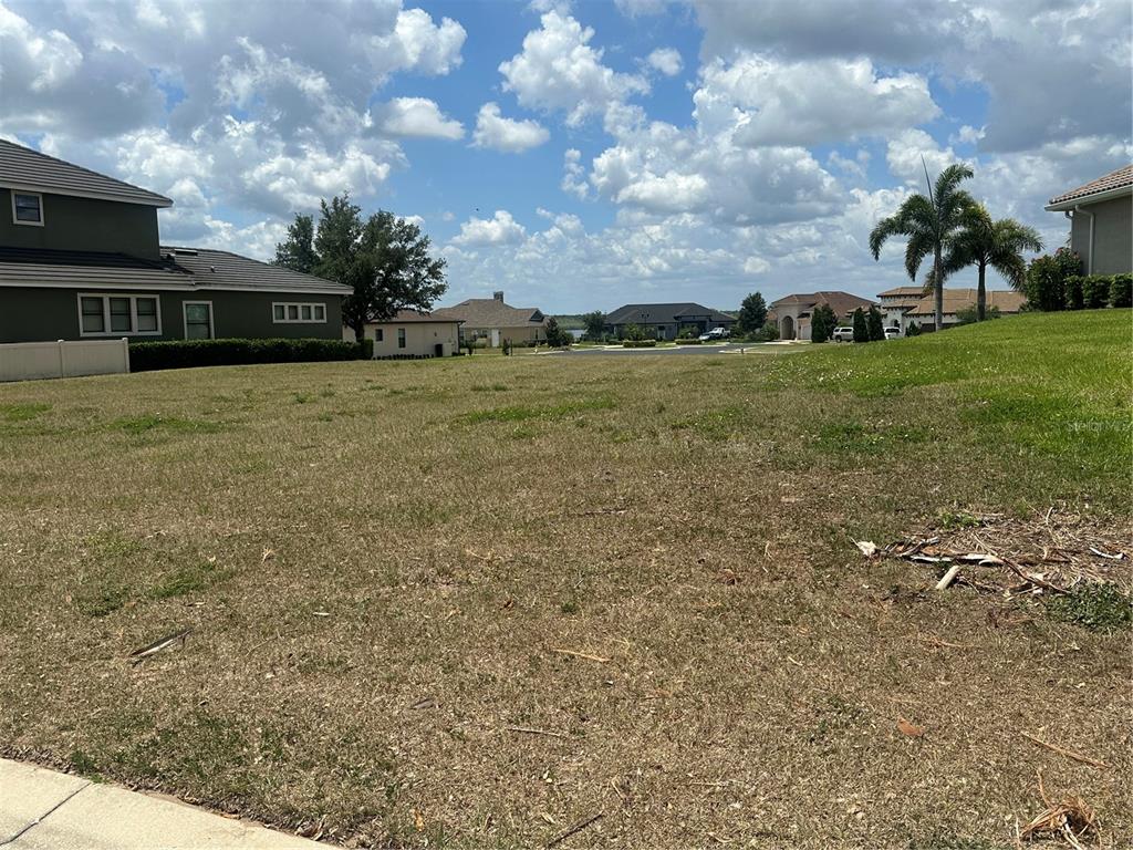 A vacant, grassy residential lot sits between two large houses under a cloudy blue sky — 126 STARGRASS DRIVE, AUBURNDALE, FL