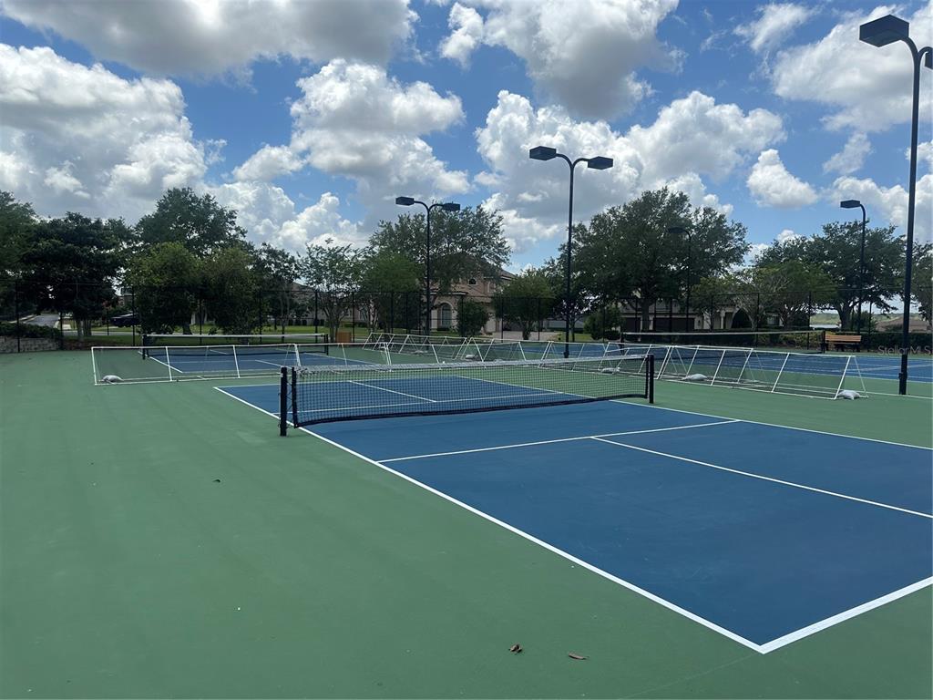 A blue and green tennis court with a net and stadium lighting under a cloudy sky — 126 STARGRASS DRIVE, AUBURNDALE, FL
