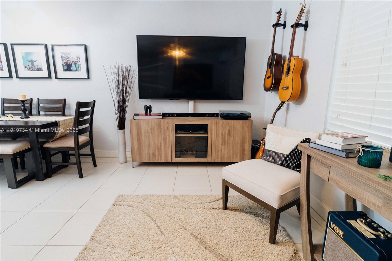 A living room features a wall-mounted television, wooden media console, and two hanging guitars — 7901 SW 64th Ave # 6, South Miami FL 33143, SOUTH MIAMI, FL