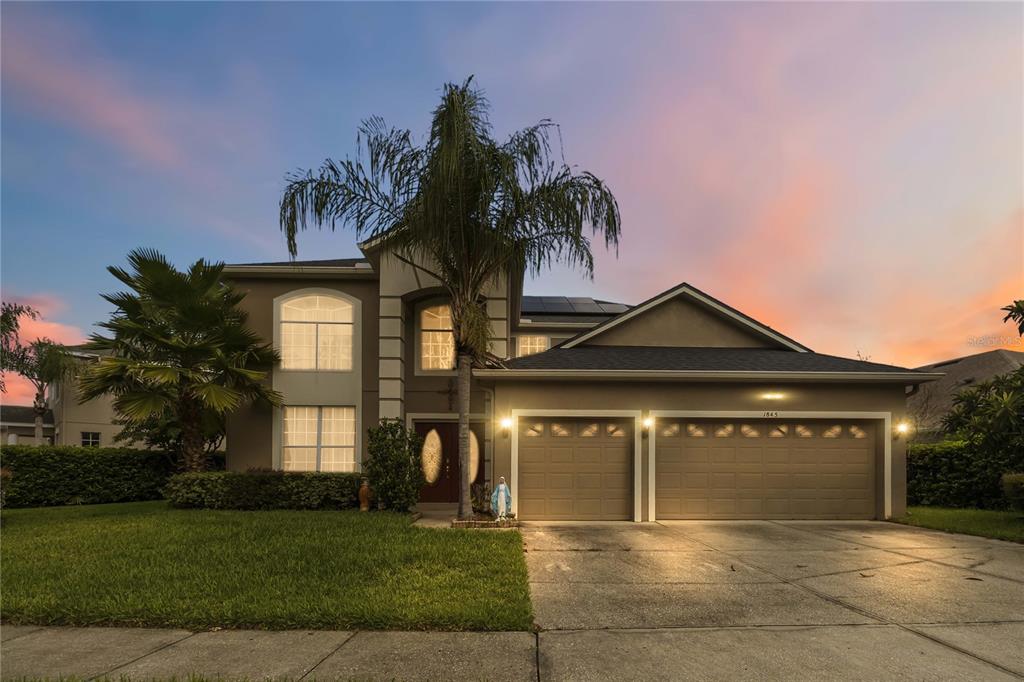 A two-story house with a two-car garage, palm trees, and a sunset sky — 1845 OAK GROVE CHASE DRIVE, ORLANDO, FL