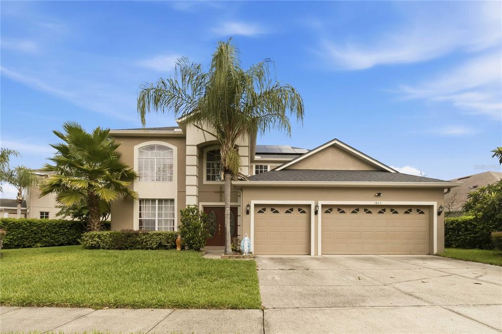 A two-story suburban house with a three-car garage, palm trees, and a concrete driveway — 1845 OAK GROVE CHASE DRIVE, ORLANDO, FL