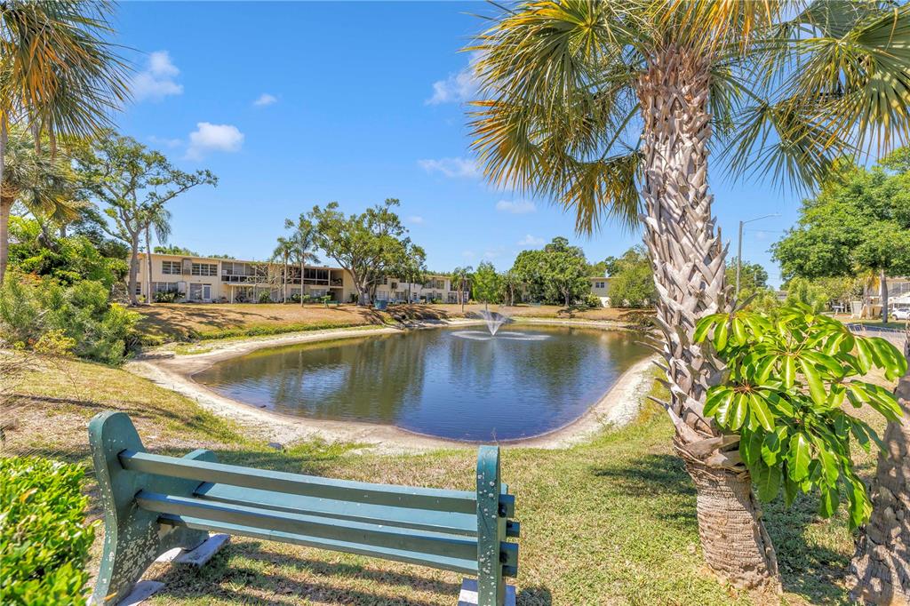 A green bench sits in the foreground overlooking a pond with a fountain and apartments — 4143 56TH STREET N UNIT 1006, KENNETH CITY, FL