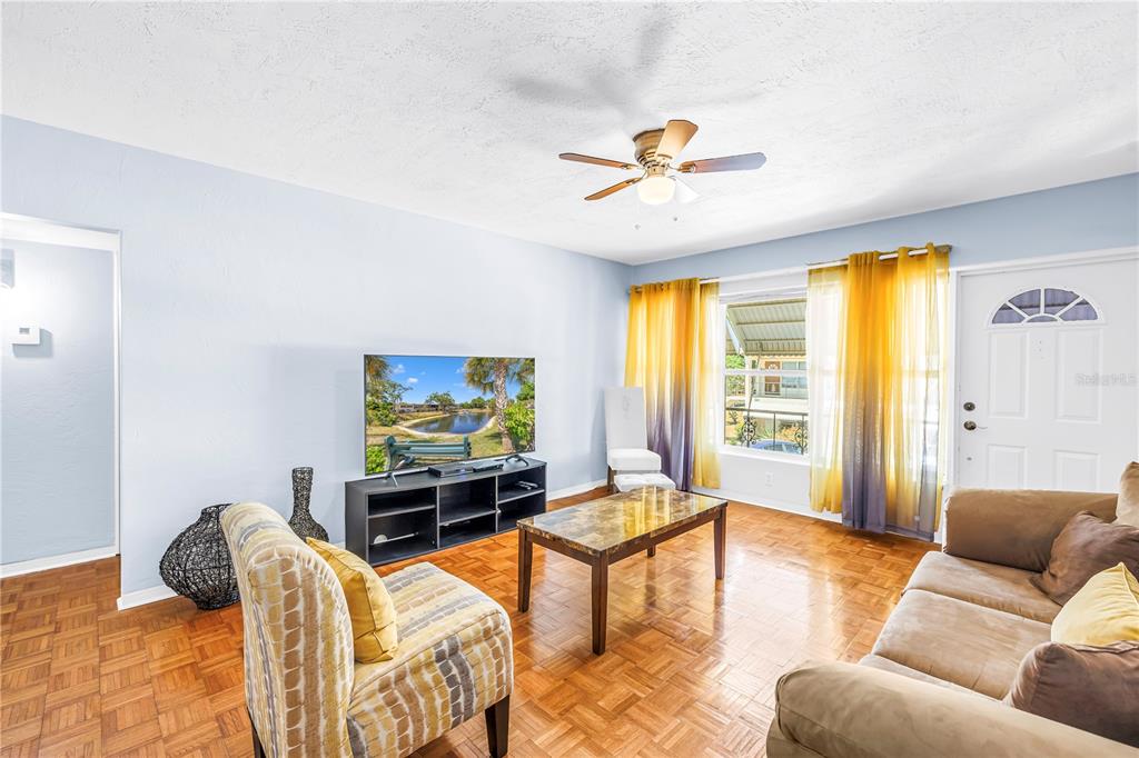 A living room features light blue walls, parquet wood flooring, a television, and yellow curtains — 4143 56TH STREET N UNIT 1006, KENNETH CITY, FL