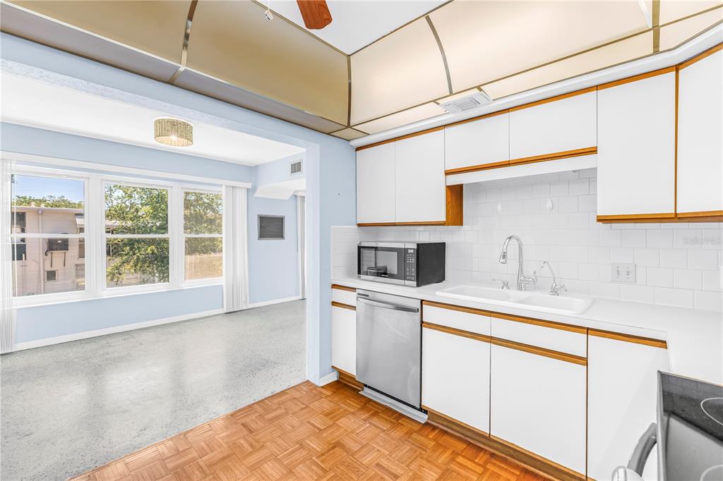 A kitchen with white cabinets, wood trim, and stainless steel appliances opens to a living area — 4143 56TH STREET N UNIT 1006, KENNETH CITY, FL