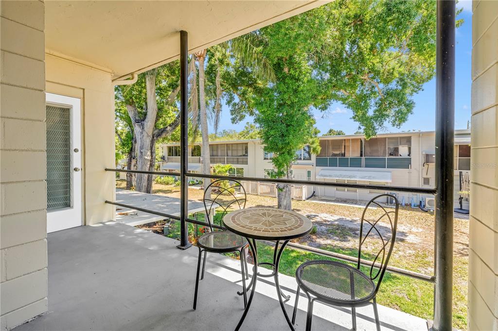 A covered balcony features a small round bistro table with two chairs overlooking a courtyard — 4143 56TH STREET N UNIT 1006, KENNETH CITY, FL