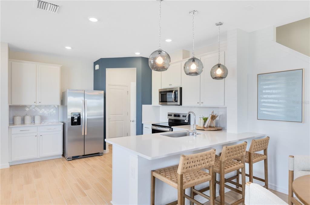 A modern kitchen features white cabinetry, stainless steel appliances, a quartz island, and pendant lighting — 4308 CHESTER SPRINGS BOULEVARD, DAVENPORT, FL