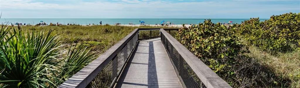A wooden boardwalk leads through coastal vegetation toward a sandy beach and the ocean — 425 CERROMAR TERRACE UNIT 359, VENICE, FL