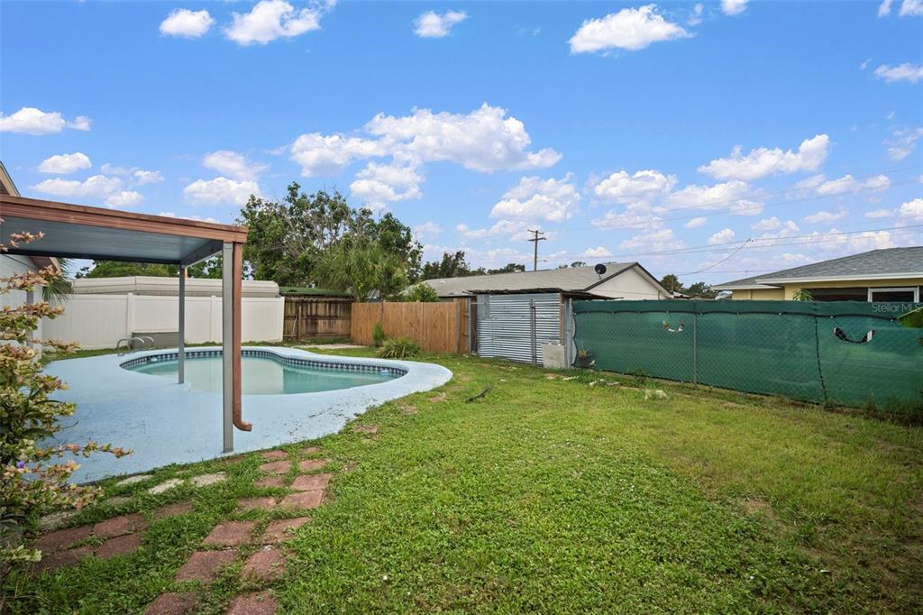 A backyard features a swimming pool with a patio cover and a green privacy screen — 4712 BESSIE ROAD, TAMPA, FL