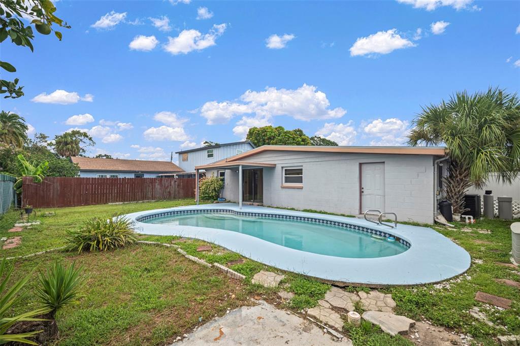 A backyard features a kidney-shaped swimming pool, a gray concrete-block house, and a wooden fence — 4712 BESSIE ROAD, TAMPA, FL